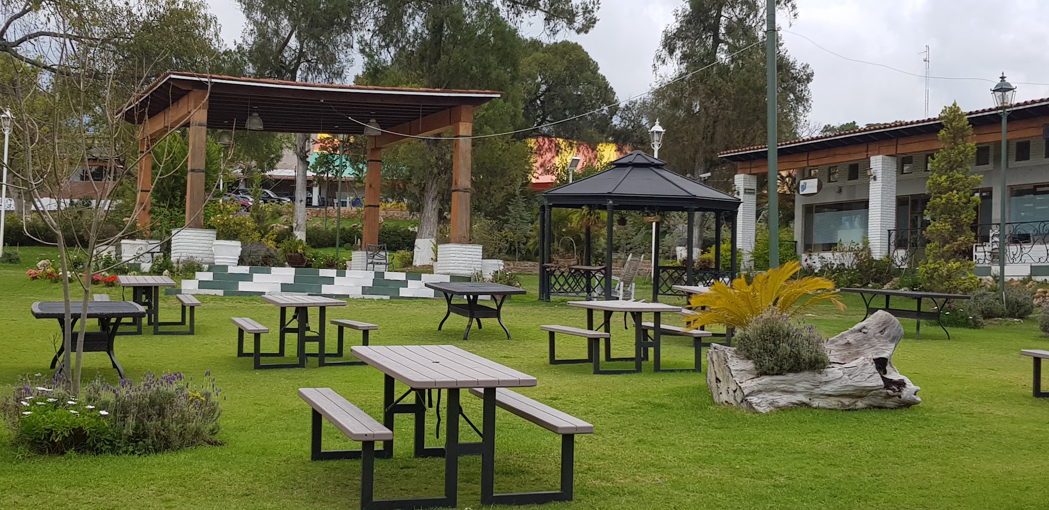A lawn with outdoor tables, a wooden shelter and garden seating at PLAZA MACLOVIA